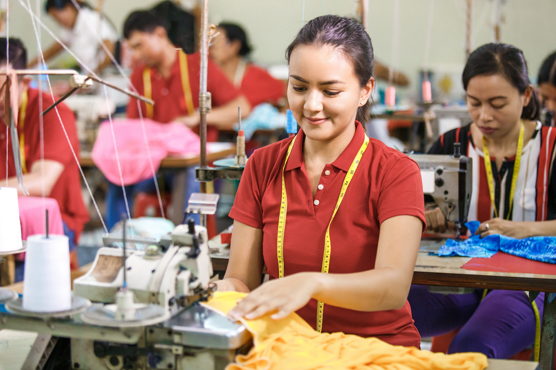 portrait of professional Seamstress in textile factory sewing with industrial sewing machine at garment